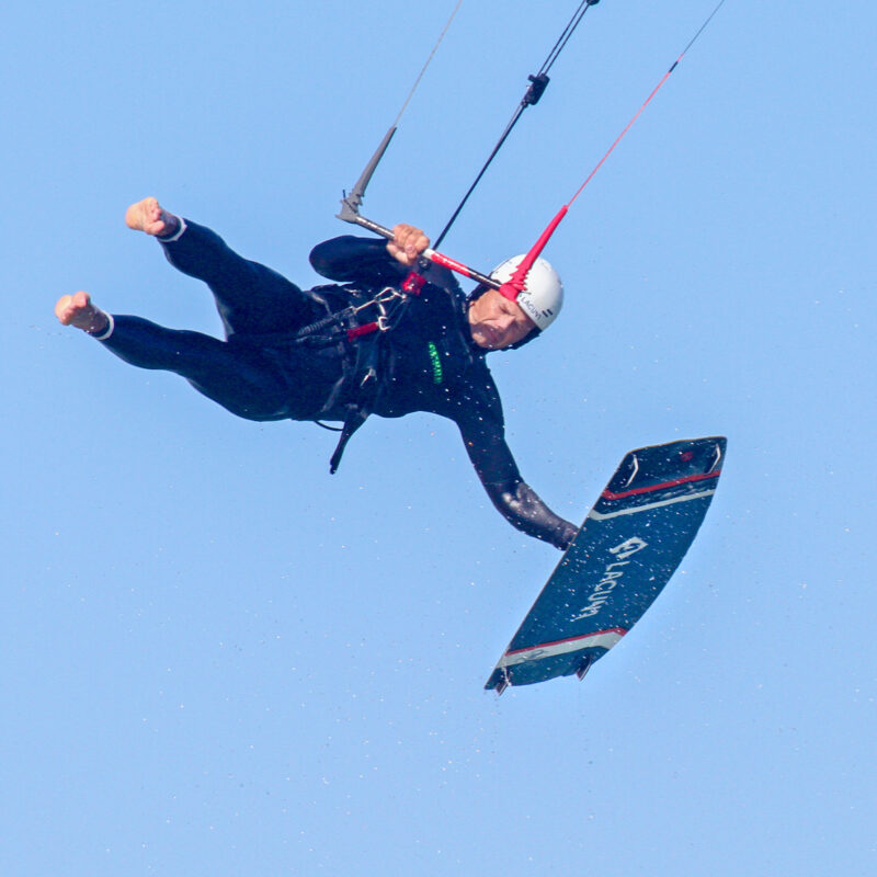 Kiteboarder with white helmet in mid air with the board in his hand
